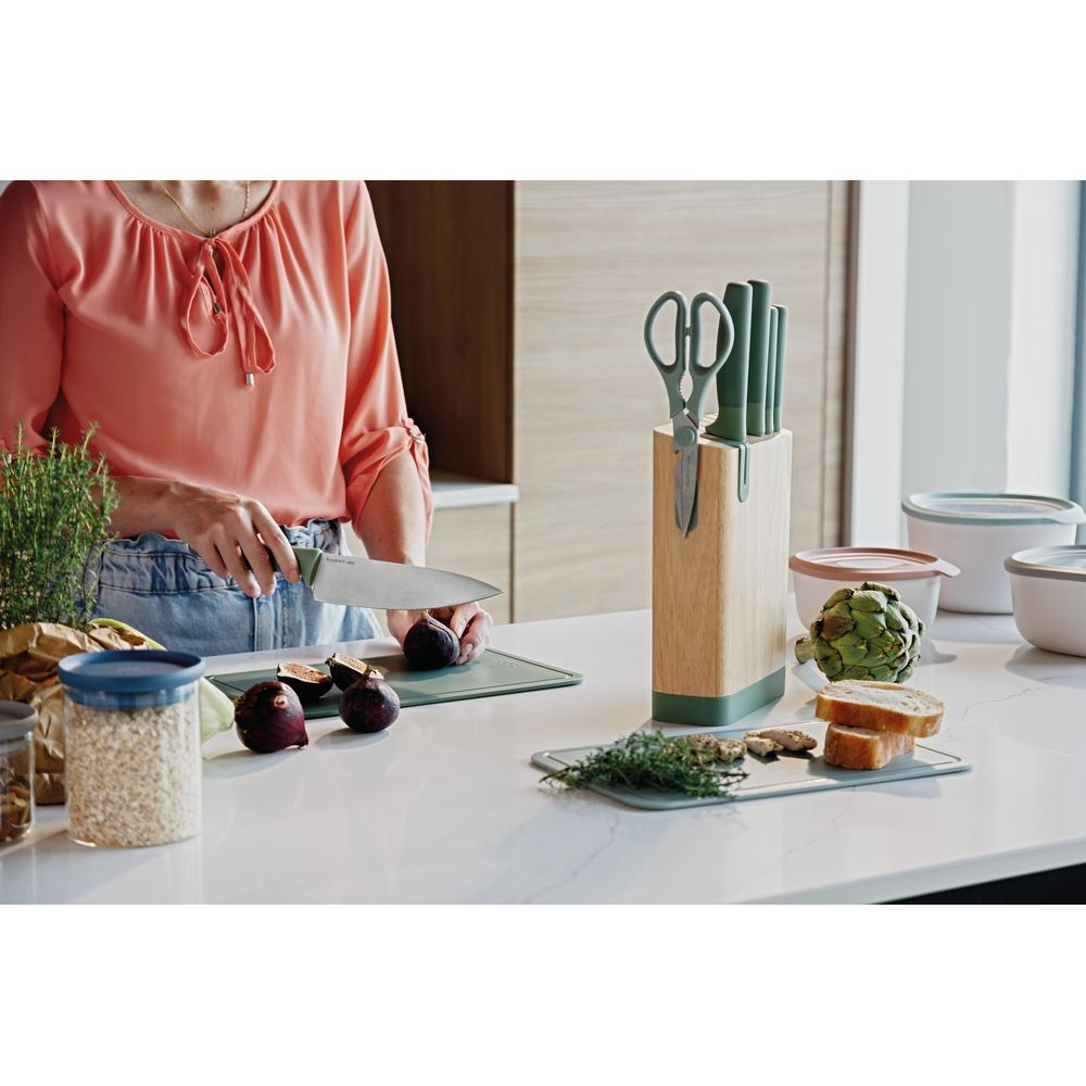 A person cuts figs on a cutting board. A knife block stands nearby.