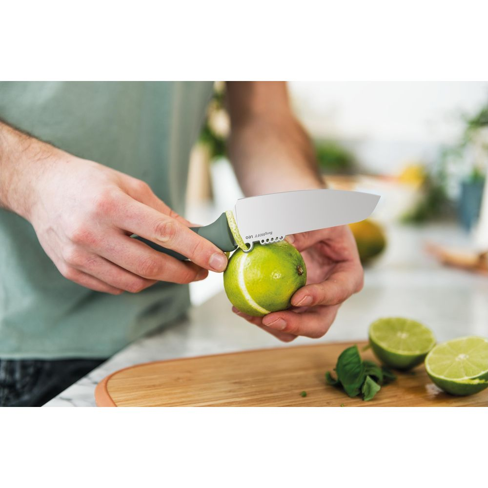 Man cuts a lime with a knife on a wooden board. Two halves lie beside it.