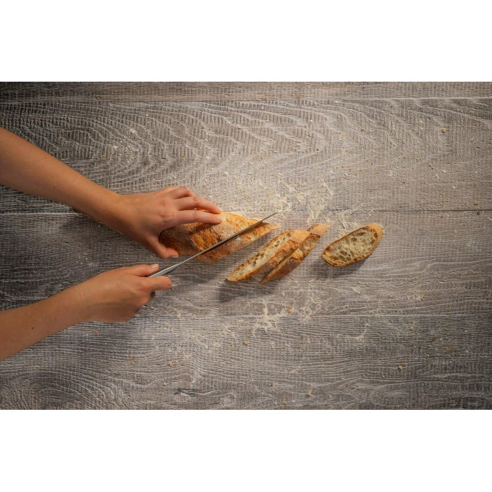 Hände schneiden ein Baguette auf einem Holztisch in Scheiben.