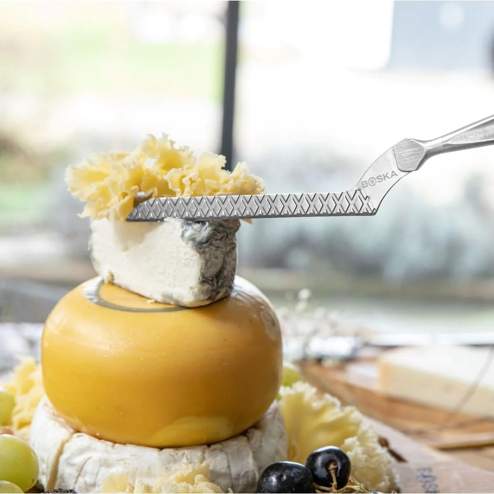 Cheese plane shaves cheese stacked on other cheeses with grapes.