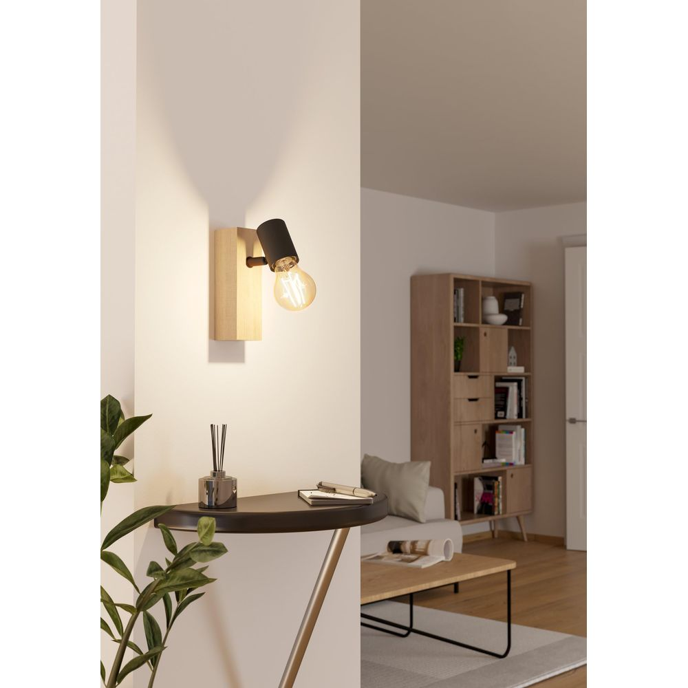 Ein Wandlicht mit Holzsockel und schwarzem Schirm beleuchtet eine Wand.