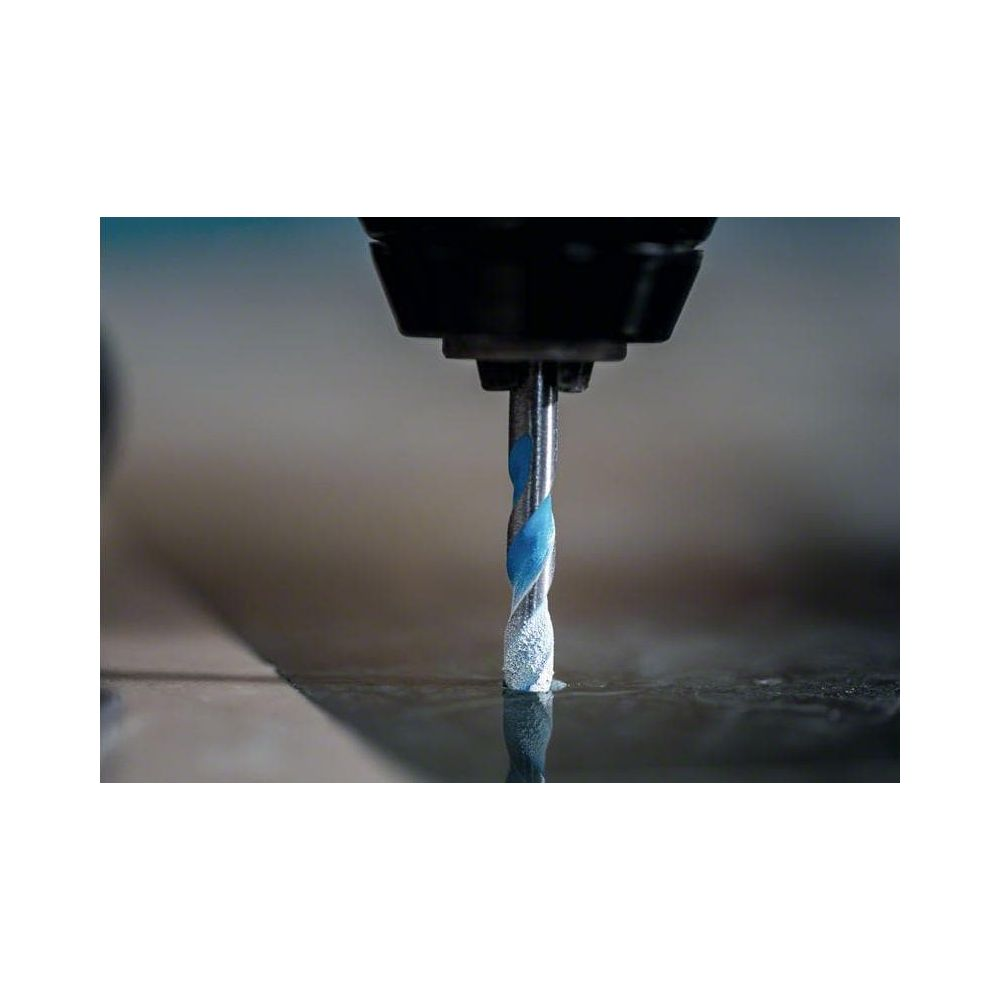 Niebieski wiertło wierci w ciemną powierzchnię, wzbija się kurz.