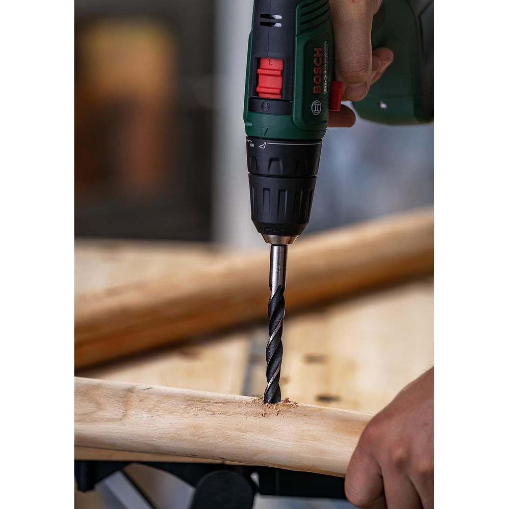 Un homme perce un trou dans un morceau de bois avec une perceuse Bosch.
