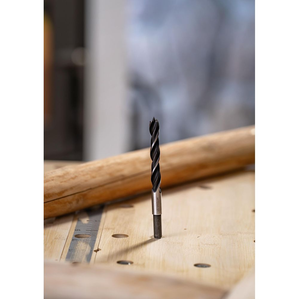 Une mèche hélicoïdale noire se dresse sur une surface en bois avec un autre objet en bois à l'arrière-plan.