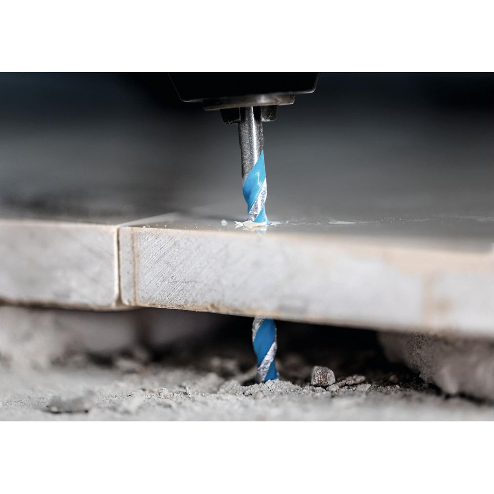 Ein blauer Bohrer bohrt durch graue Fliesen, Staub wird aufgewirbelt.