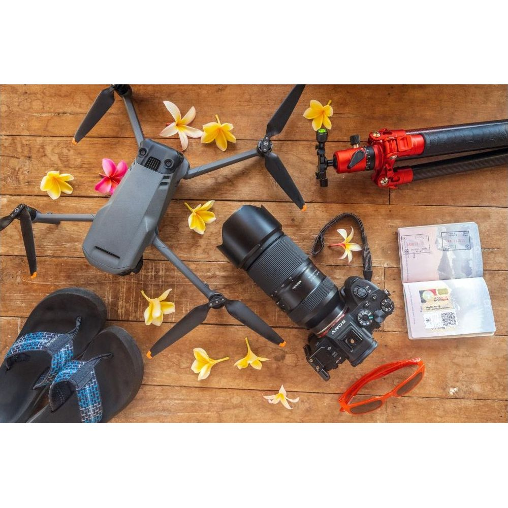 Dron, aparat fotograficzny, paszport, okulary przeciwsłoneczne, kwiaty i klapki na drewnie.