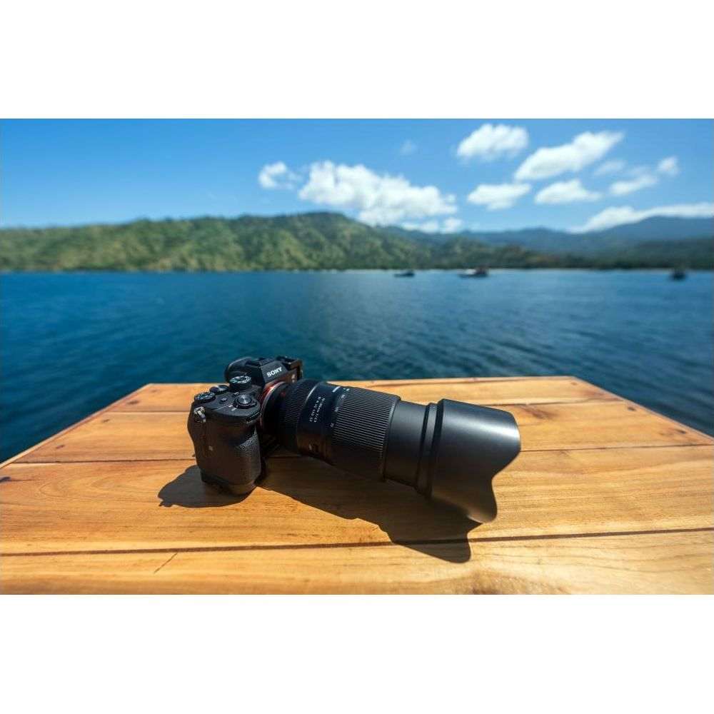 Aparat Sony z długim obiektywem leży na drewnianym stole nad morzem.