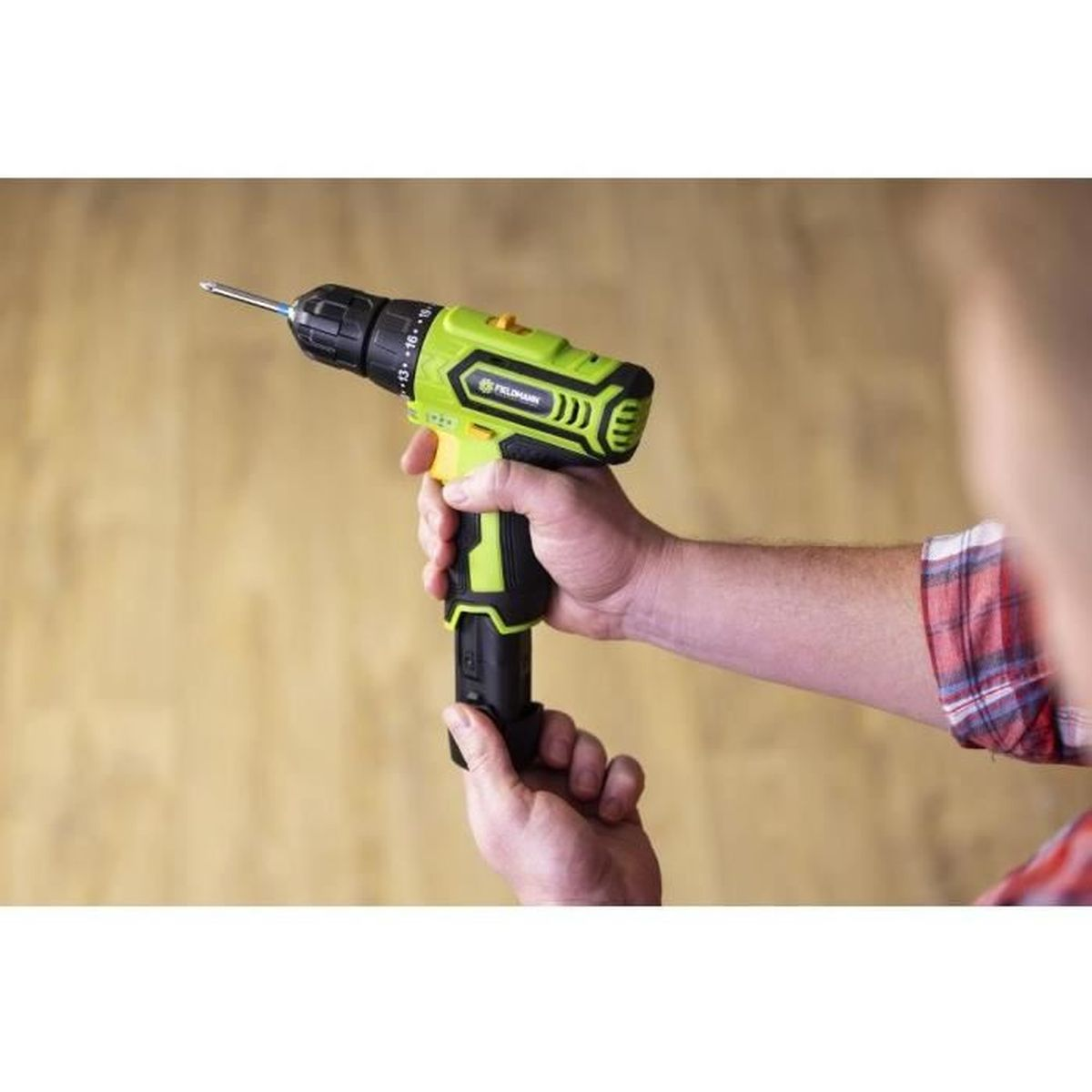 Osoba trzyma zielono-czarną wkrętarkę akumulatorową na tle drewna.