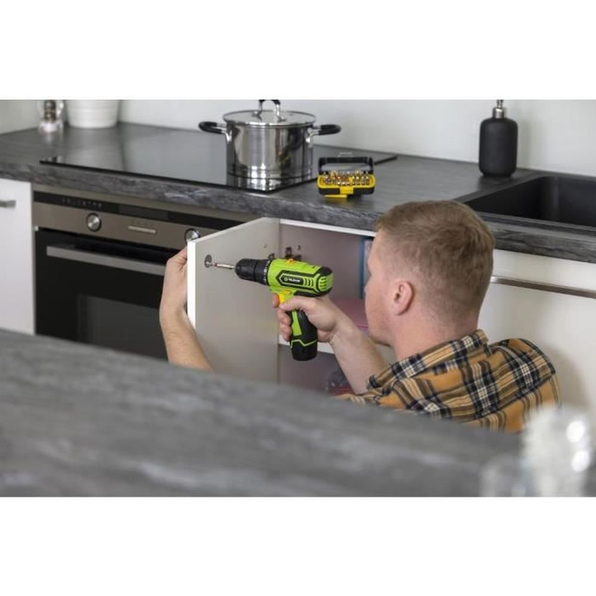 Mężczyzna naprawia drzwi szafki zielonym wiertarko-wkrętarką.