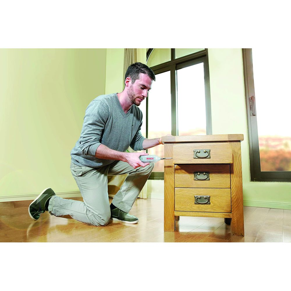 Un homme utilise une petite perceuse pour visser dans une armoire en bois à trois tiroirs.
