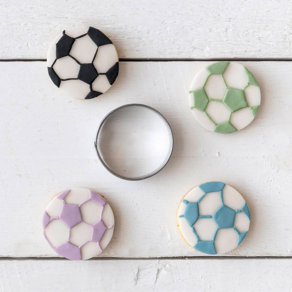 Quatre biscuits en forme de ballon de foot avec accents noir, vert, violet, bleu sur table bois.