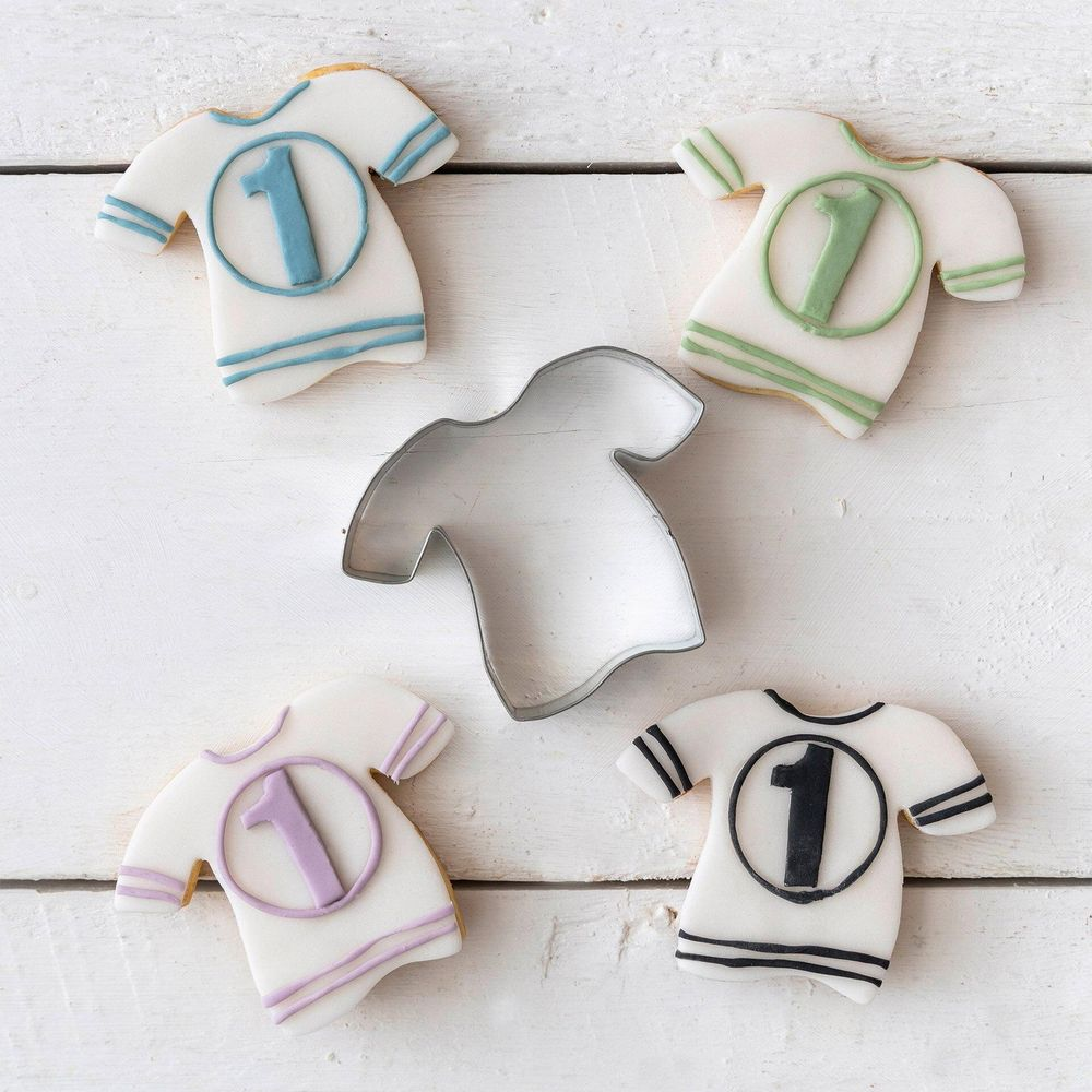 Un emporte-pièce en forme de t-shirt et quatre biscuits en forme de t-shirt avec le chiffre 1.