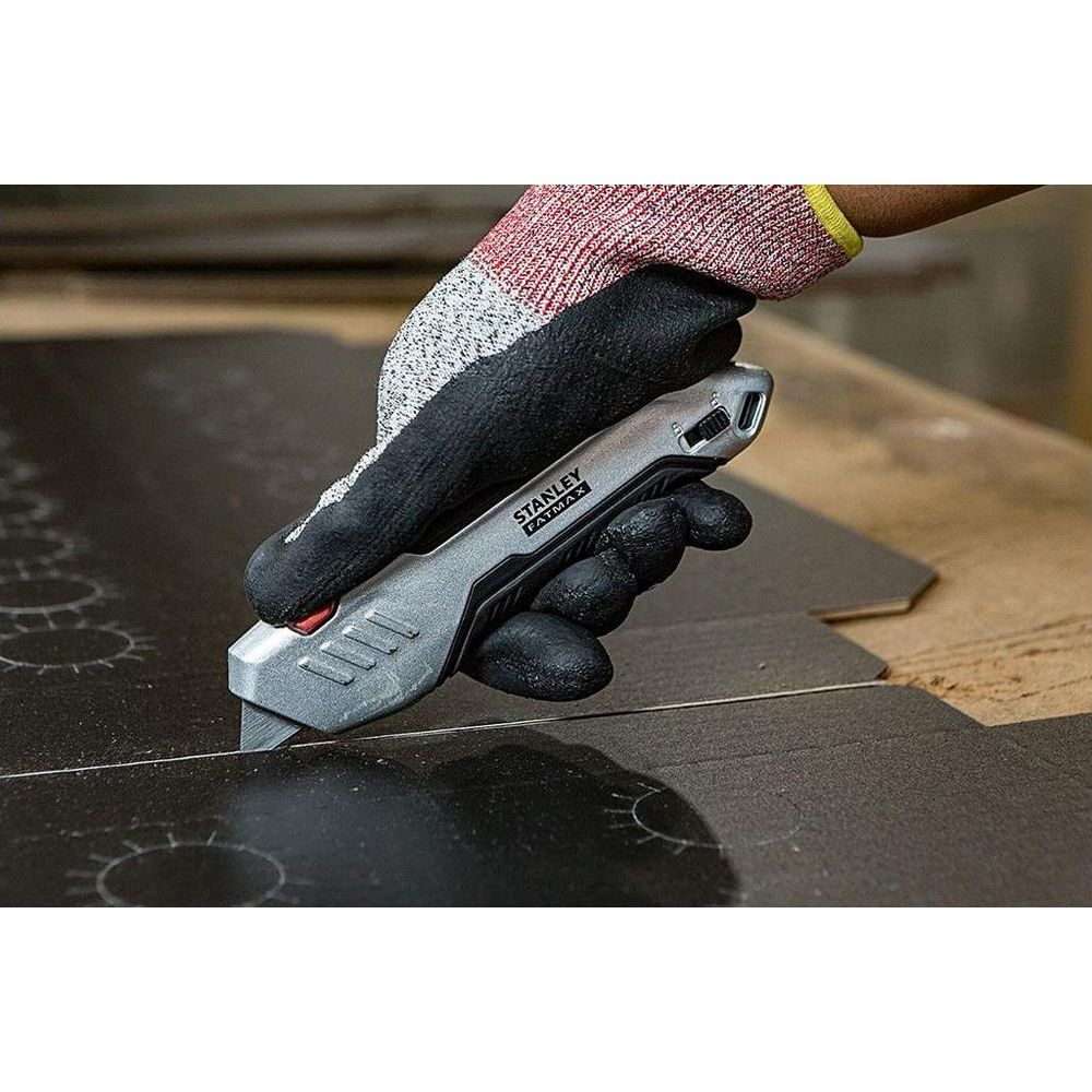 Eine Hand mit Handschuhen schneidet mit einem Stanley-Messer auf schwarzem Material.