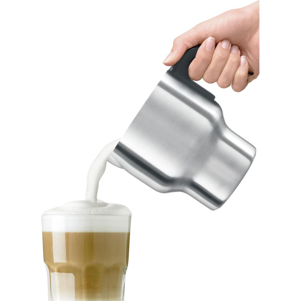 Una mano versa latte montato da una caraffa in metallo in un bicchiere di caffè.