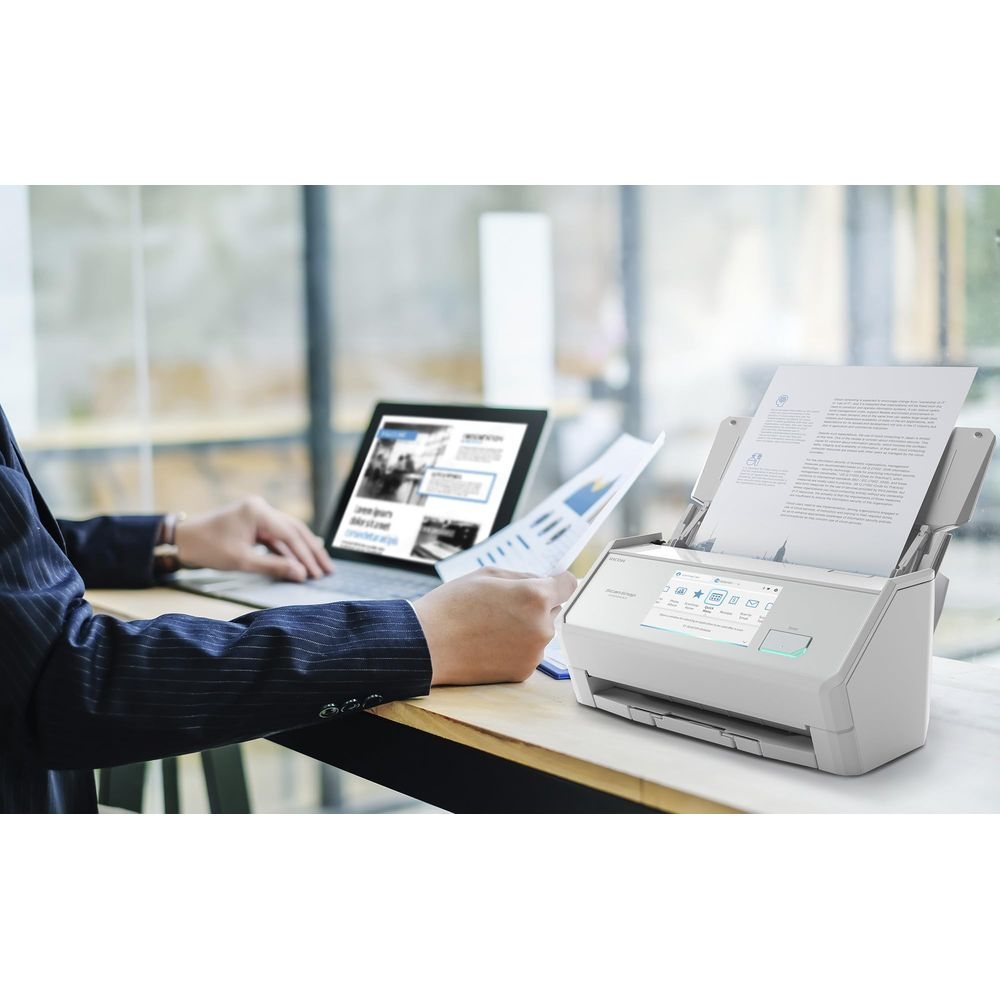 Een man scant documenten met een witte scanner, laptop en tablet op de achtergrond.