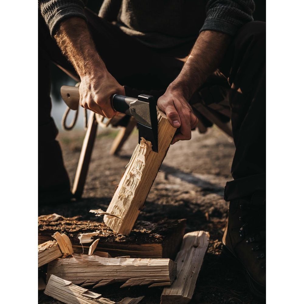 Mann spaltet Holz mit einer Axt im Freien. Detailaufnahme der Hände und des Werkzeugs.