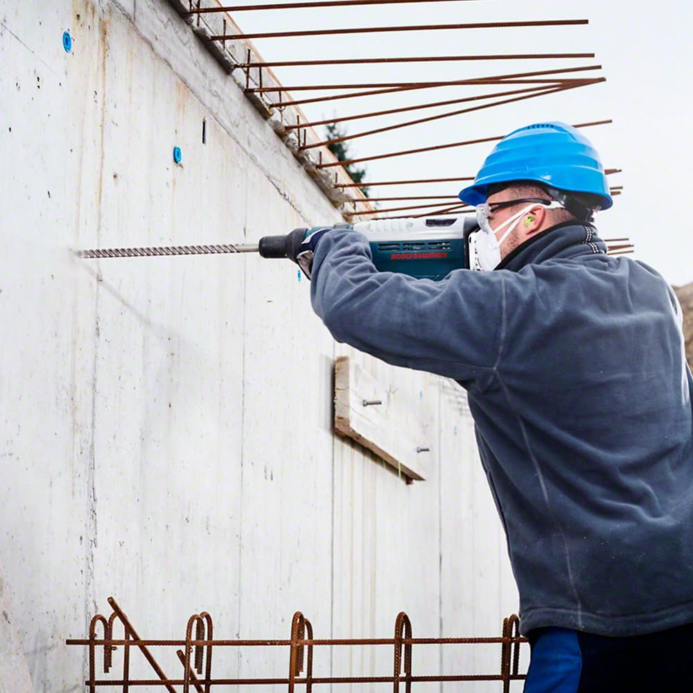 Uomo fora muro in cemento con trapano a percussione, casco blu.