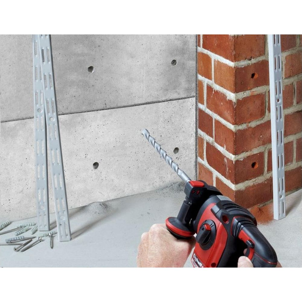 Un hombre perfora un agujero en una pared de hormigón con un taladro percutor. Hay tornillos cerca.