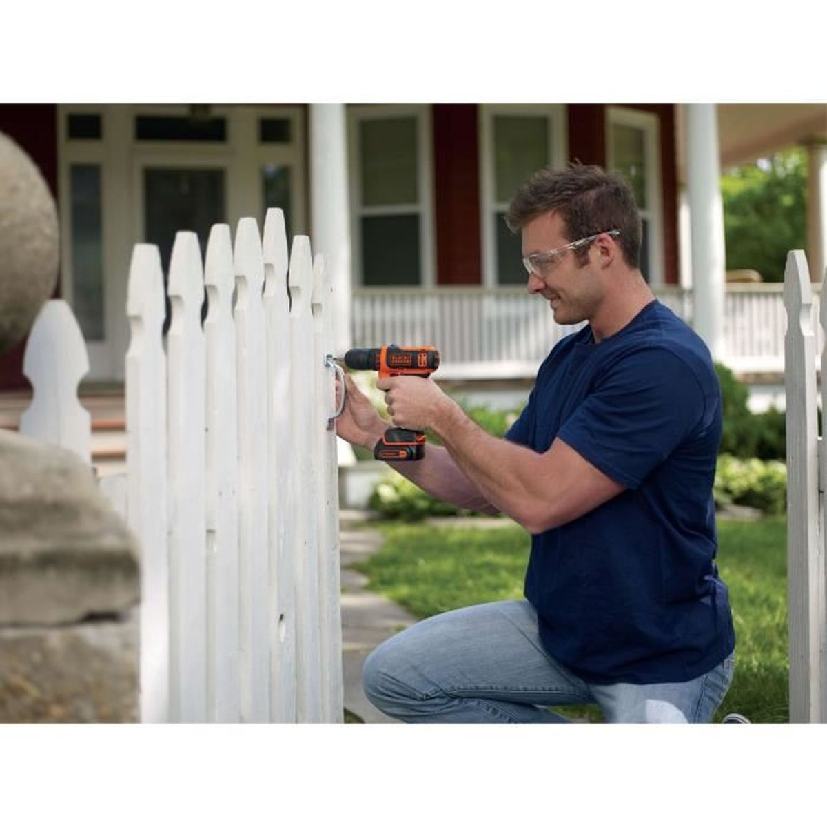 Mężczyzna wierci w białym płocie wkrętarką, nosi okulary ochronne.