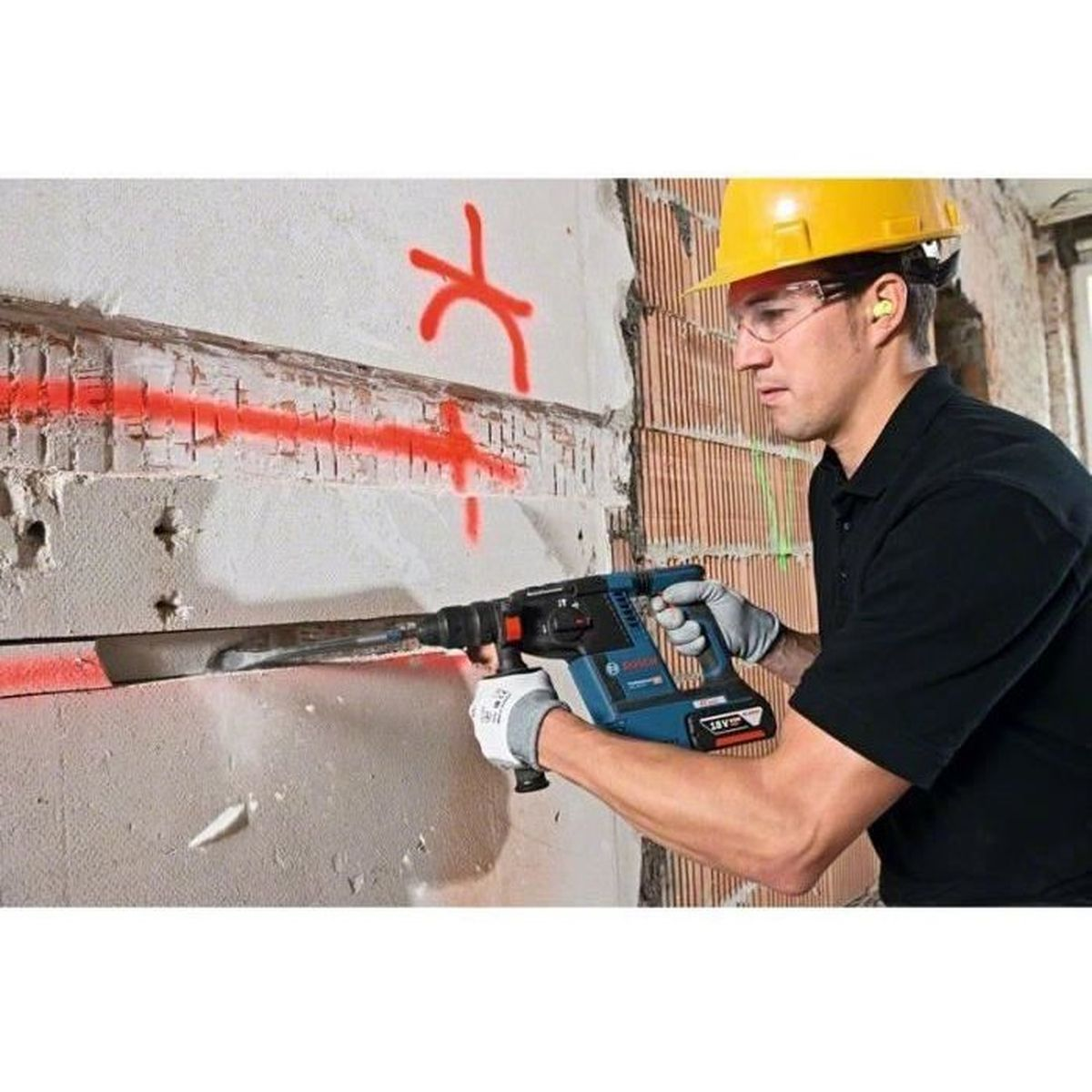 Mann mit Bohrmaschine arbeitet an Wand mit roter Markierung.