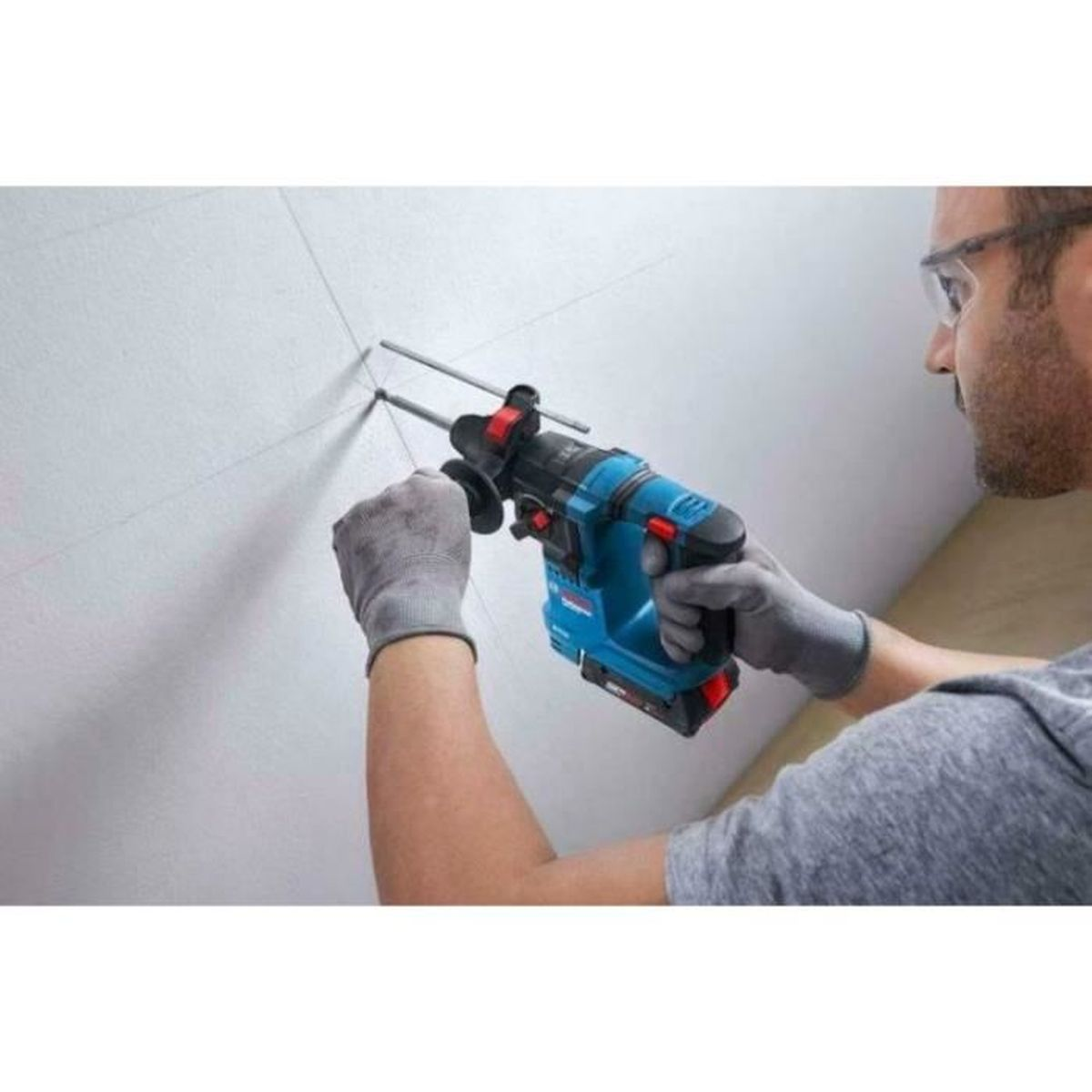 Mann bohrt mit blauem Schlagbohrer in weiße Decke. Graue Handschuhe.