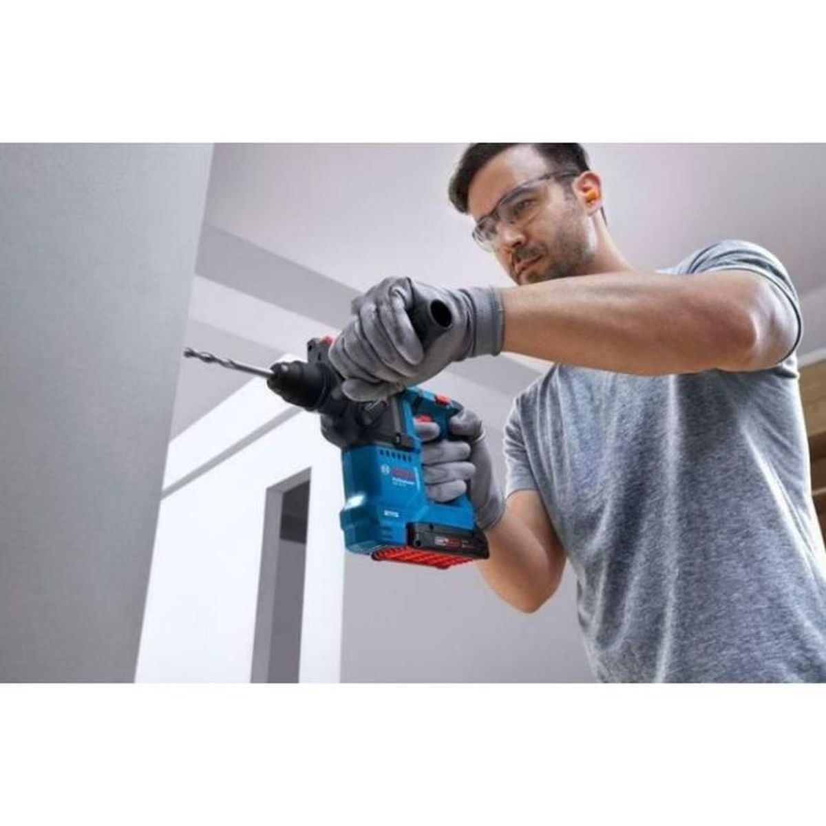 Mann mit Schutzbrille bohrt mit Schlagbohrmaschine in Wand.