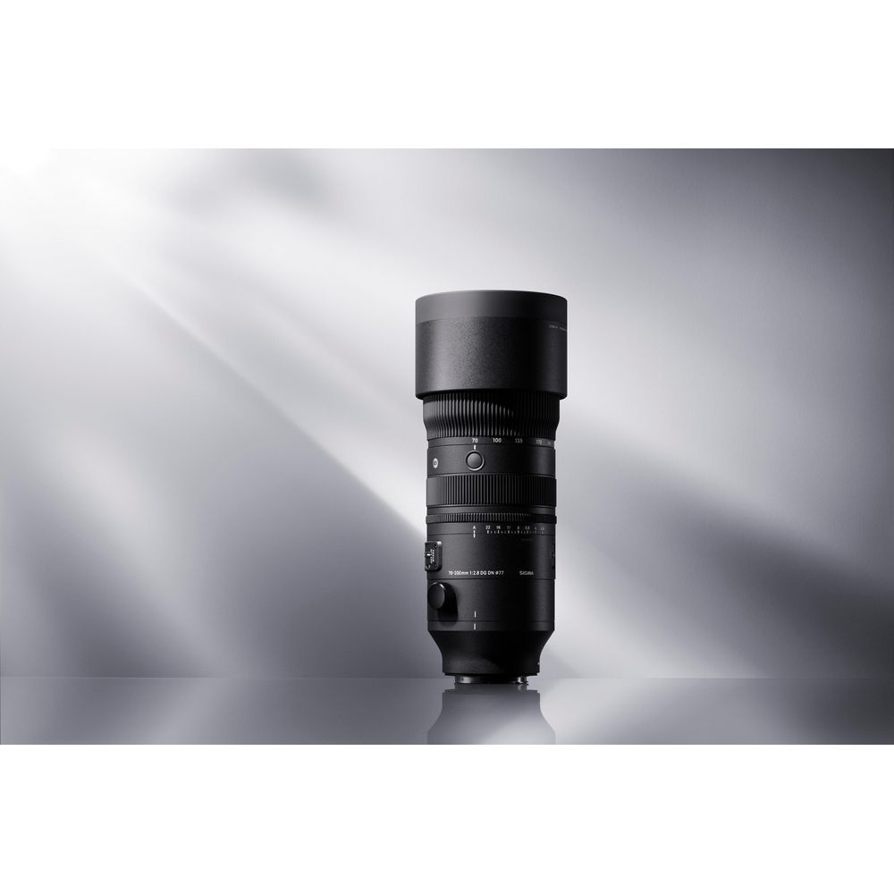 Ein schwarzes Sigma 70-200mm Objektiv steht auf einer spiegelnden Fläche vor einem grauen Hintergrund.