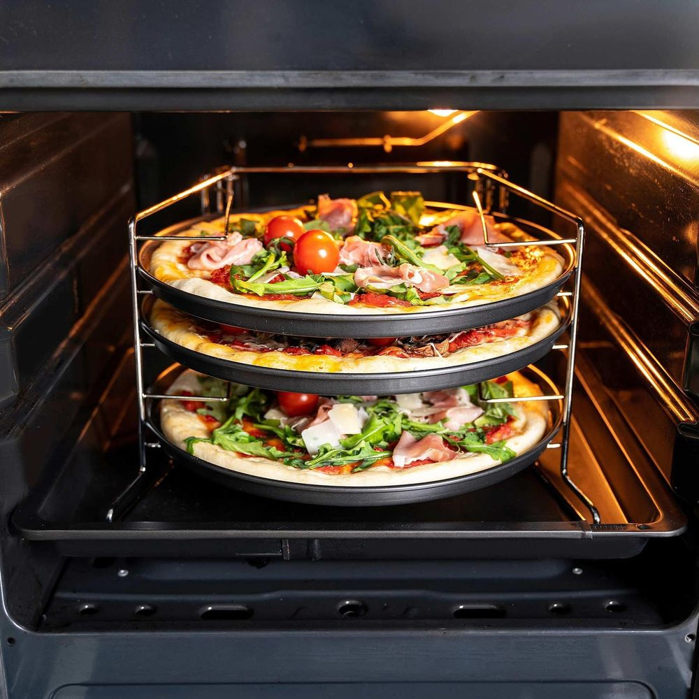 Drei Pizzen mit Tomaten und Rucola werden in einem Ofen auf einem dreistufigen Rost gebacken.
