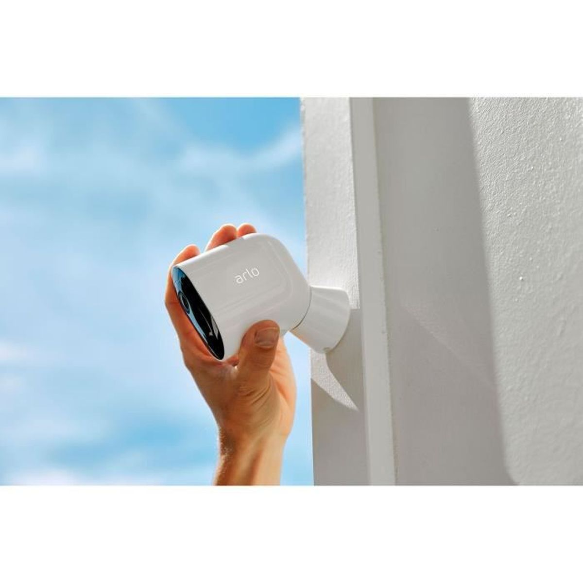 Una telecamera Arlo bianca viene montata su un muro bianco con cielo blu sullo sfondo.