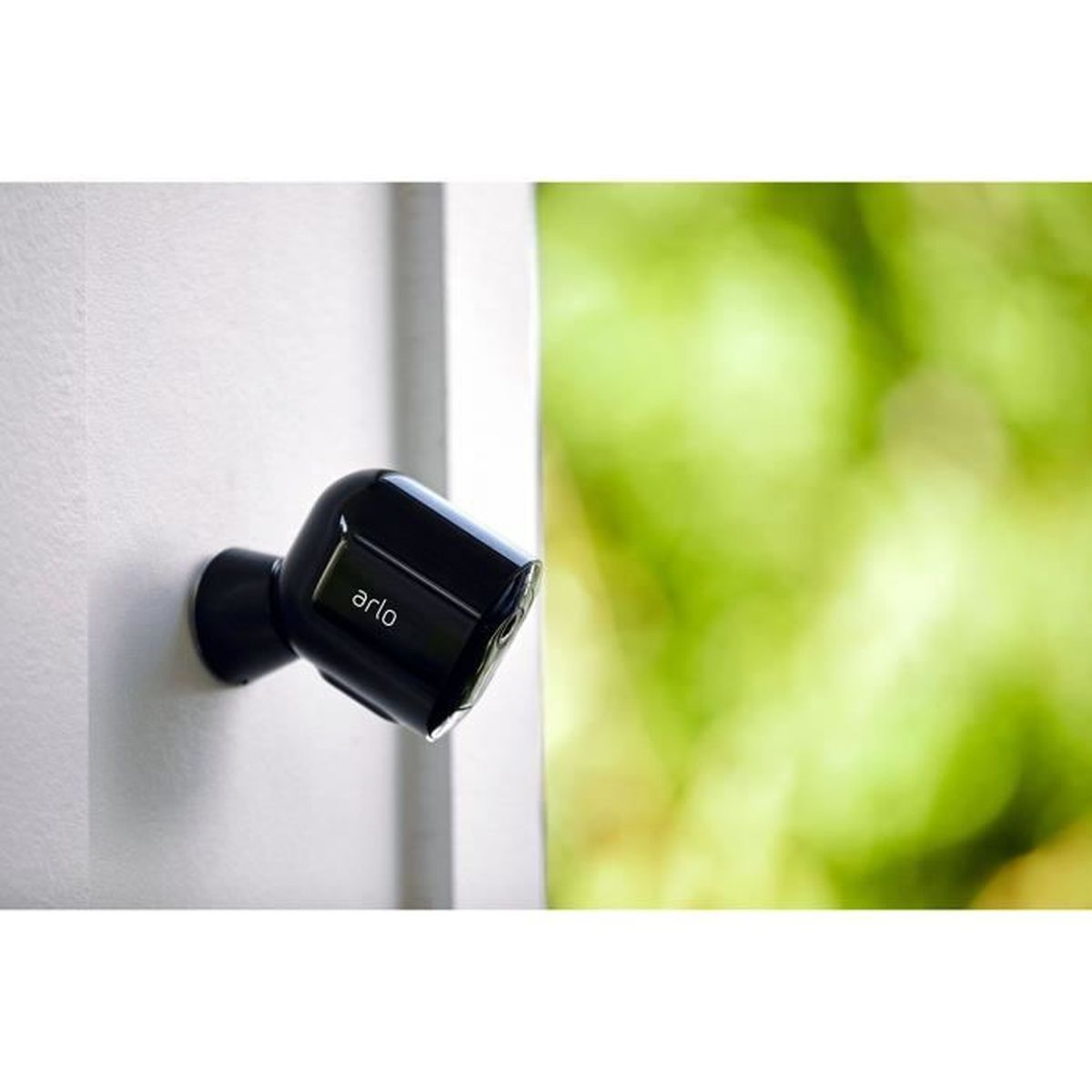 Una telecamera Arlo nera è montata su un muro bianco, con verde sfocato sullo sfondo.