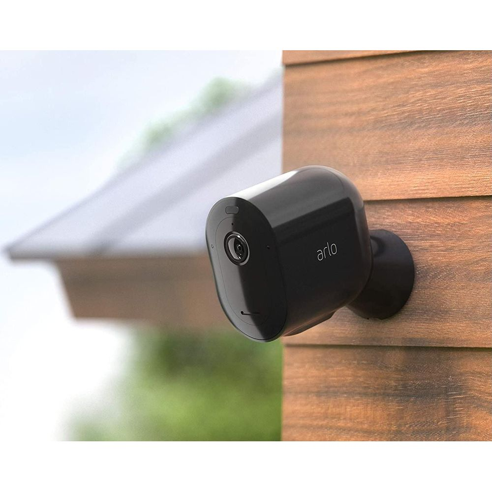 Telecamera Arlo nera montata su rivestimento in legno, con tetto sullo sfondo.