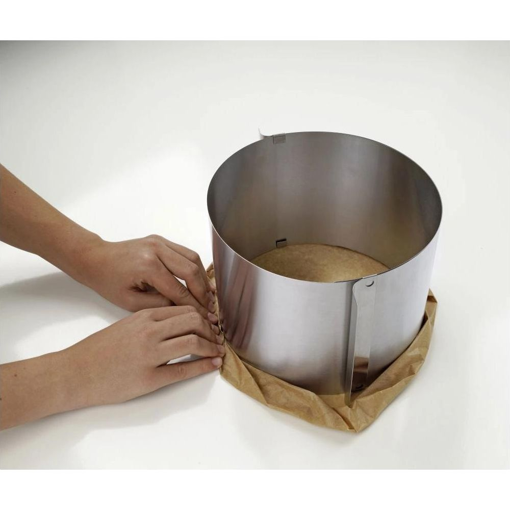 Hände legen Backpapier um einen Metallring für Kuchen.