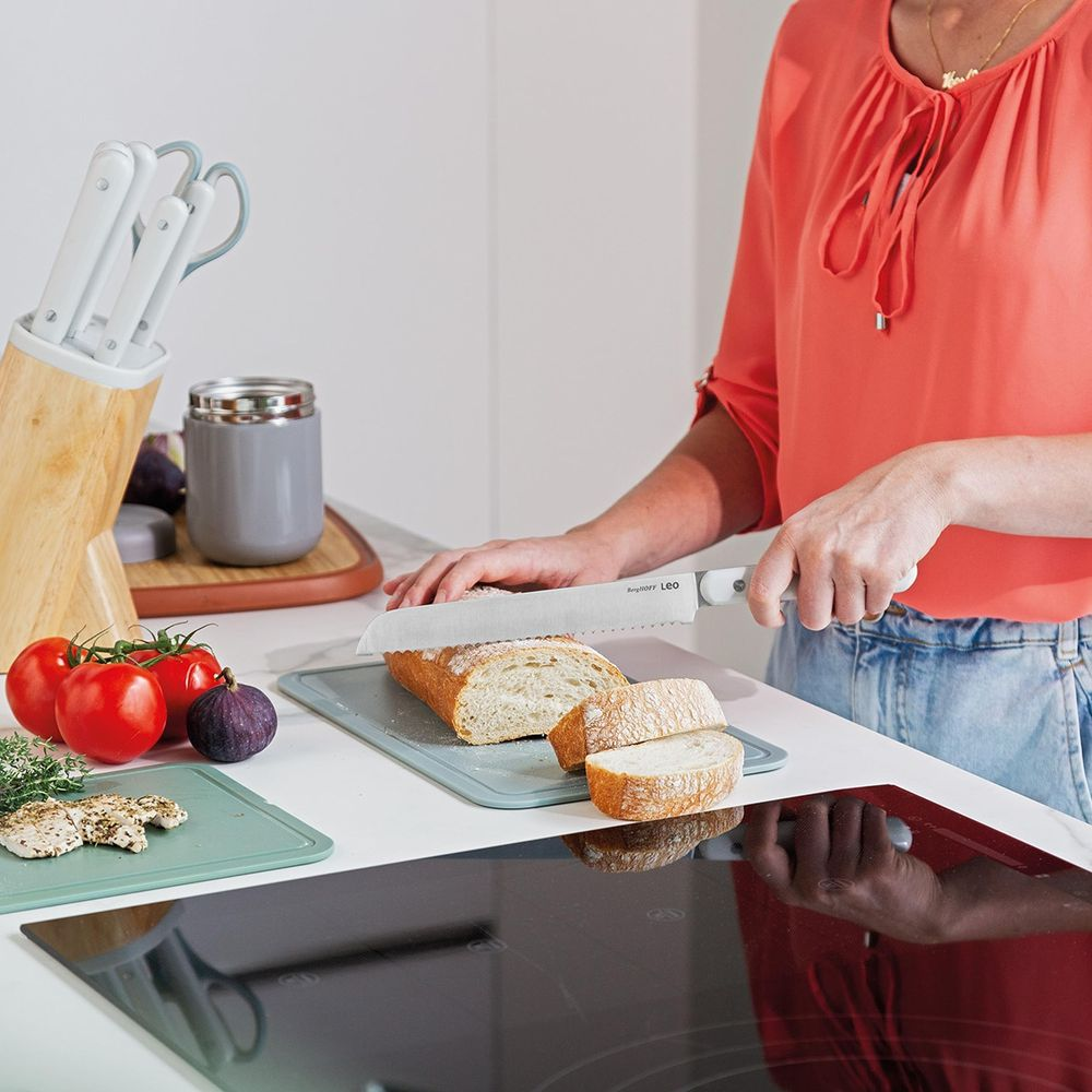 A person is slicing bread in a kitchen with a knife.