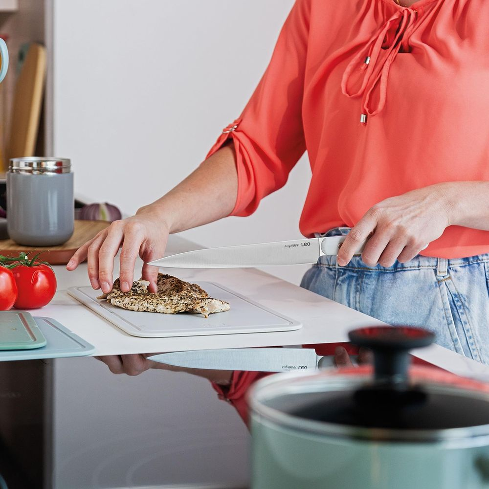 Person slicing cooked chicken on a cutting board with a knife.