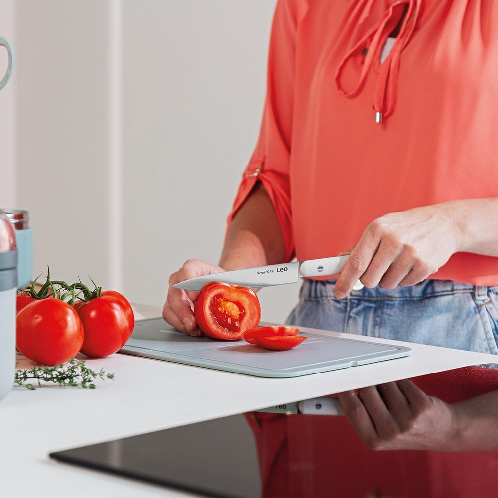 A person is slicing a tomato on a cutting board in the kitchen.