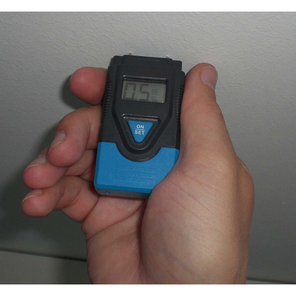 Ein Mann hält einen digitalen Feuchtigkeitsmesser, der 0,5 % anzeigt.