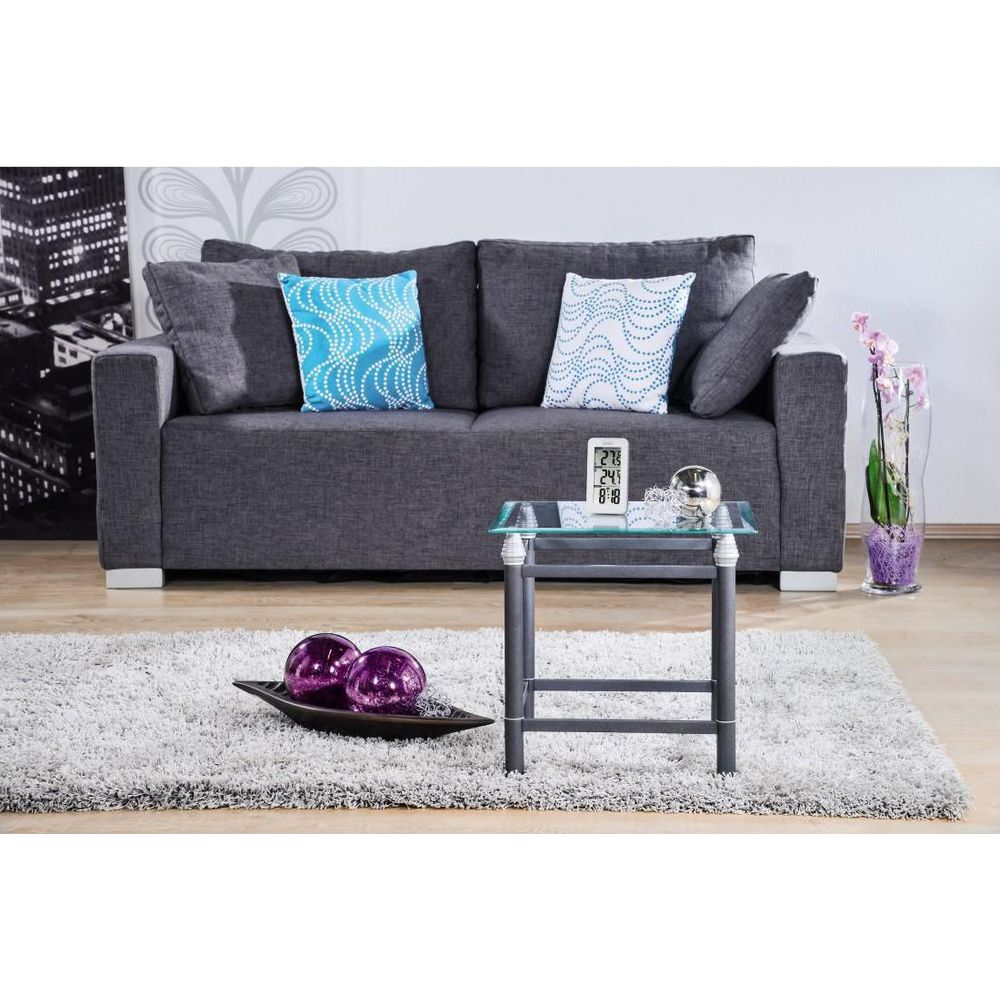 Ciemna sofa z poduszkami i szklany stolik z dekoracjami.