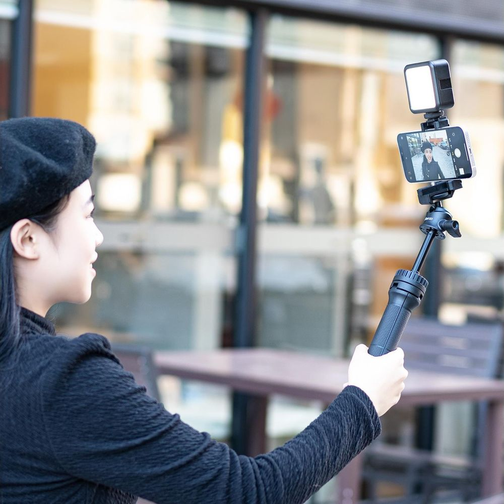 Kobieta w czarnym beretem robi sobie selfie telefonem przymocowanym do selfie sticka z lampką.