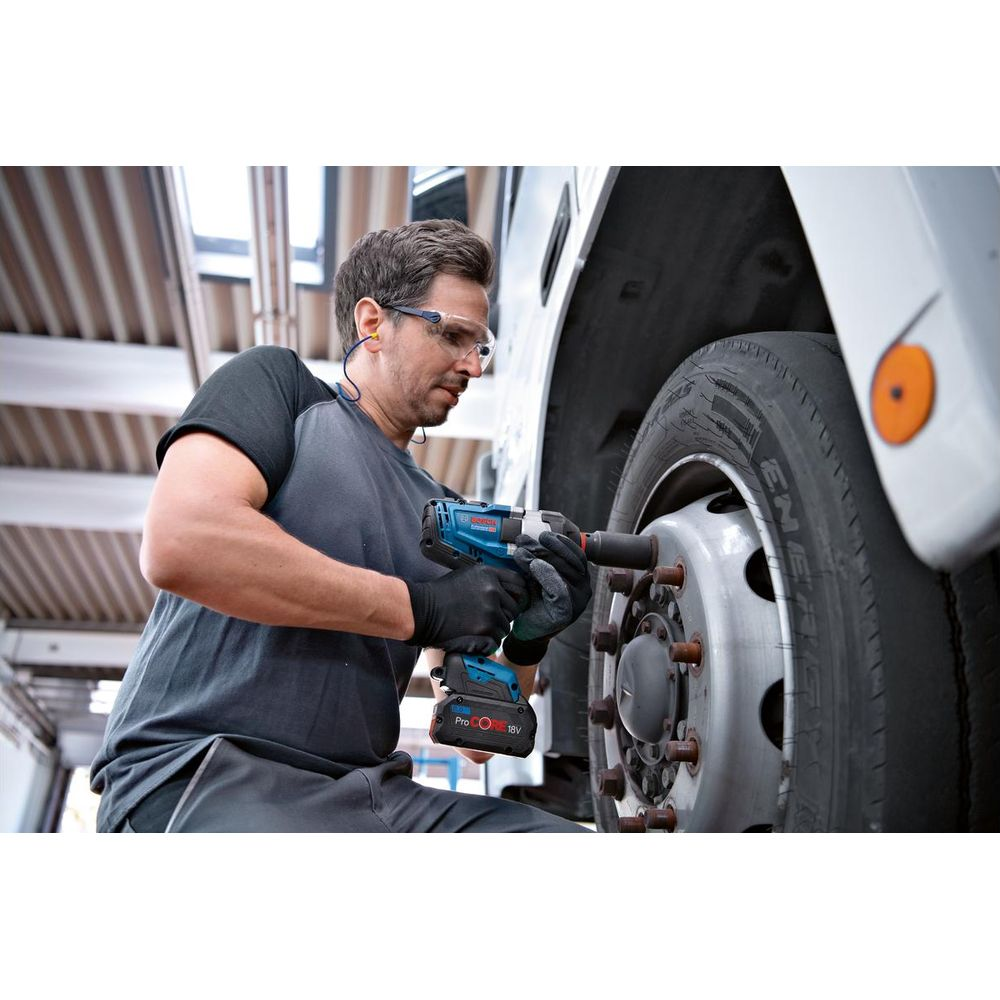 Mężczyzna w okularach ochronnych używa niebieskiego klucza udarowego do koła ciężarówki.