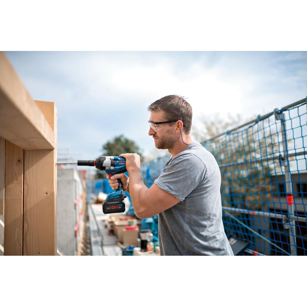 Mężczyzna w okularach ochronnych używa wiertarko-wkrętarki na drewnianej ramie.