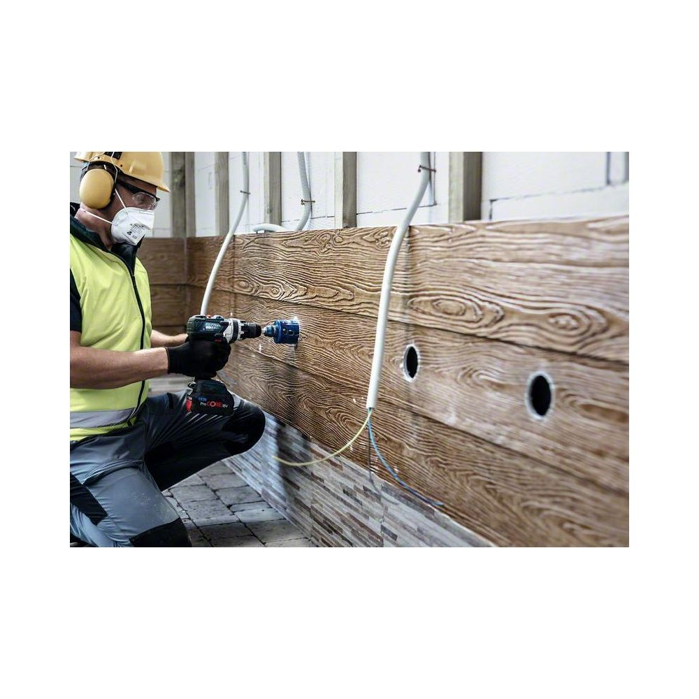 Robotnik budowlany wierci otwór w drewnianej ścianie w kasku.