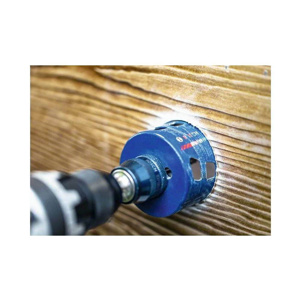 Niebieska otwornica Bosch wierci otwór w drewnie.