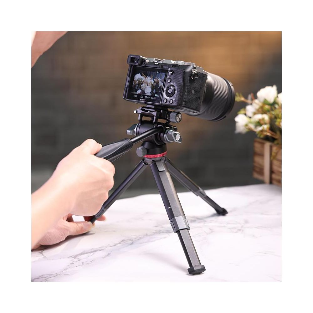 Ręka reguluje aparat na statywie, w tle kwiaty.