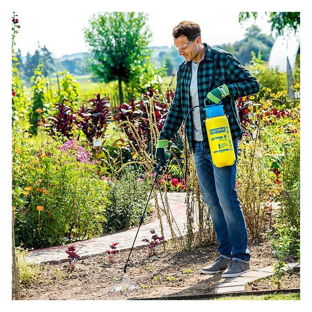 Mężczyzna spryskuje rośliny żółtym opryskiwaczem w bujnym ogrodzie.