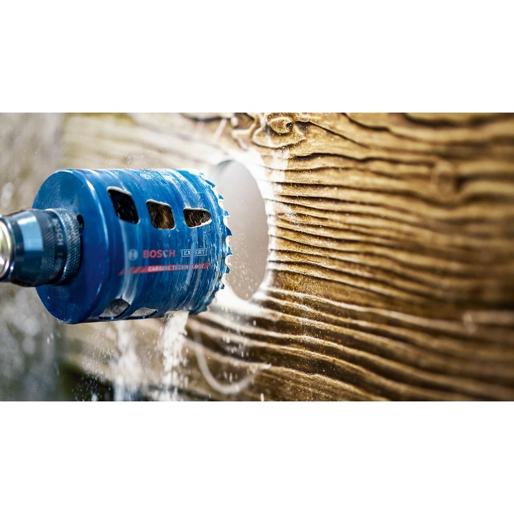 Niebieski wiertło Bosch przecina otwór w drewnie. Pył leci.