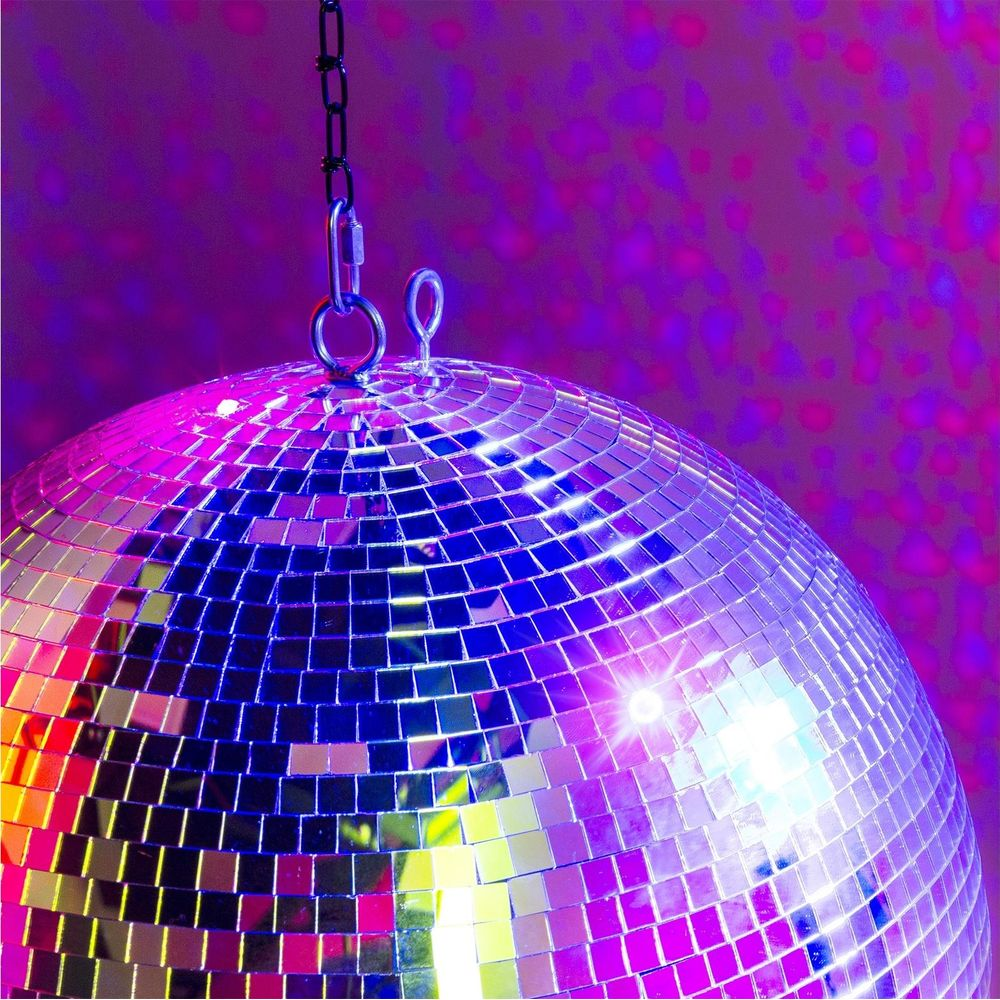 Una bola de discoteca brillante cuelga de una cadena, iluminada por luz púrpura y rosa.