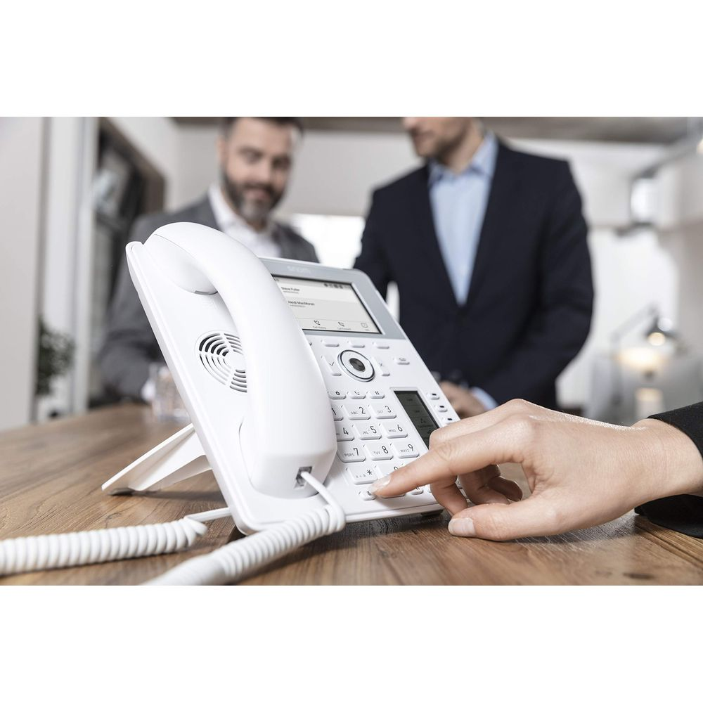 Dłoń naciska przycisk białego telefonu biurowego, dwaj mężczyźni w tle.