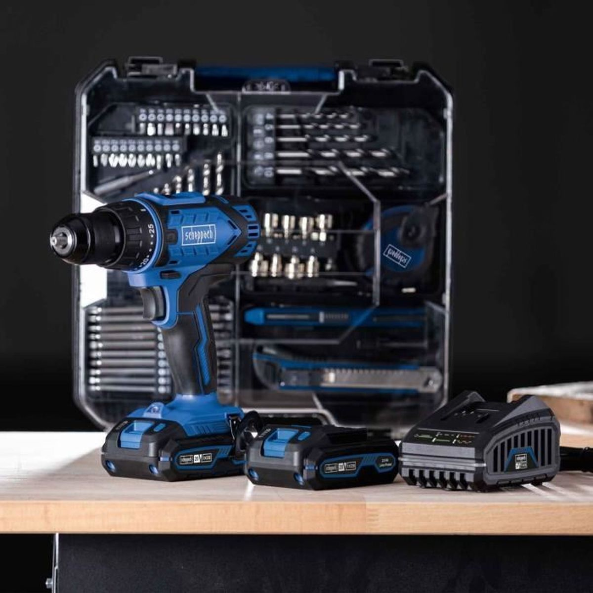 Blauwe boormachine met gereedschapskist, batterijen en lader op houten tafel.
