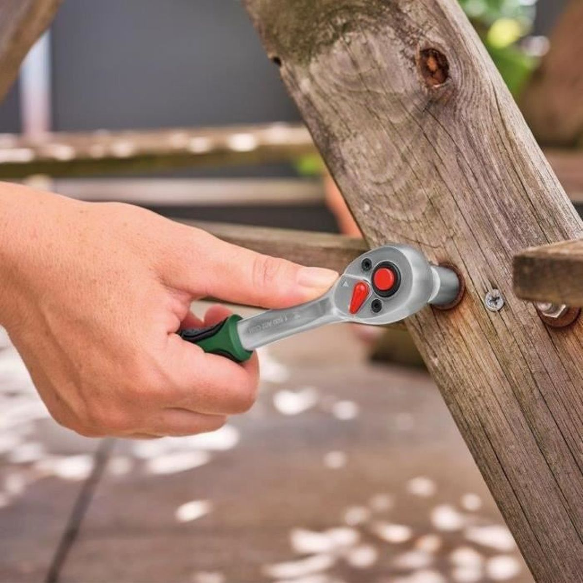 Eine Hand benutzt eine Ratsche, um eine Schraube an Holz zu befestigen.