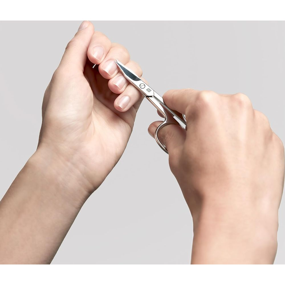 Jedna ręka używa małych nożyczek do przycinania paznokcia drugiej ręki.